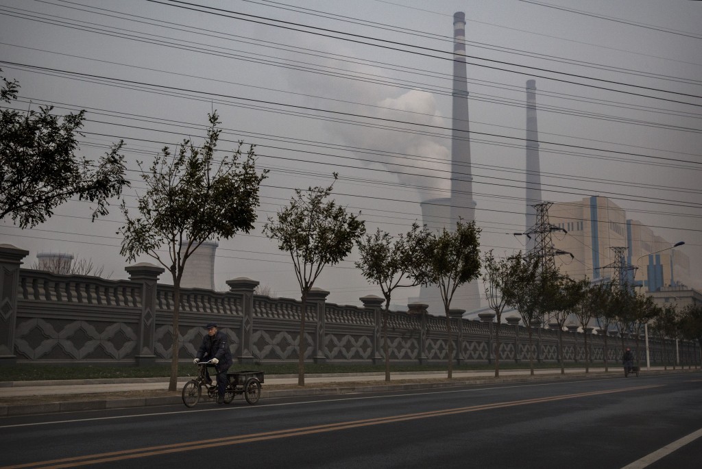 A man rides a bicycle as a coal-fired power plant in Beijing is seen in the background in a November 2014 photo..  Photo by Kevin Frayer/Getty Images.